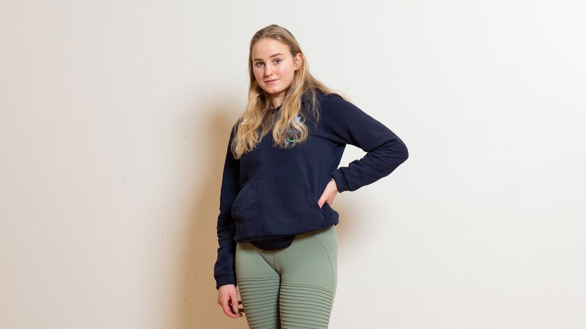 Laura Kangasniemi poseeraamassa kameralle tummansininen Paran huppari ja vihreät treenilegginssit päällään.